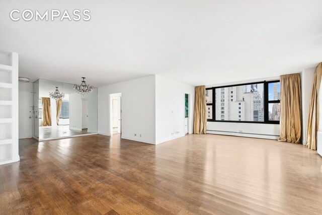 unfurnished living room featuring hardwood / wood-style floors, a notable chandelier, and baseboard heating