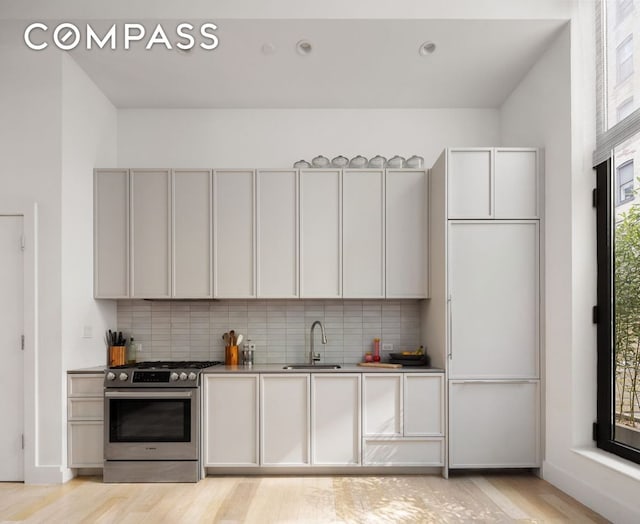 kitchen with tasteful backsplash, light wood-style flooring, stainless steel gas stove, and a sink