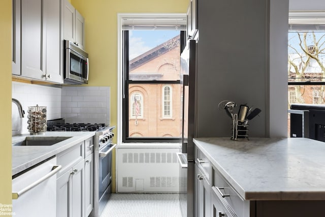 kitchen featuring sink, light stone counters, tasteful backsplash, radiator heating unit, and stainless steel appliances