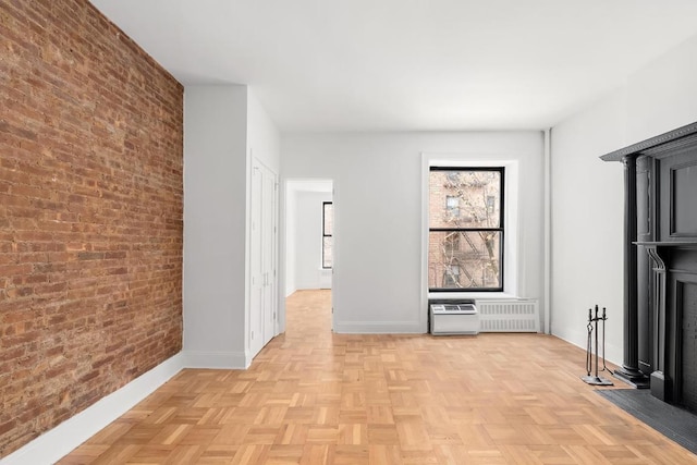 unfurnished living room featuring light parquet flooring, brick wall, and radiator heating unit