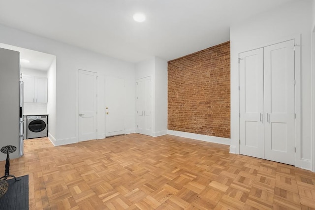 spare room featuring washer / clothes dryer, light parquet flooring, and brick wall