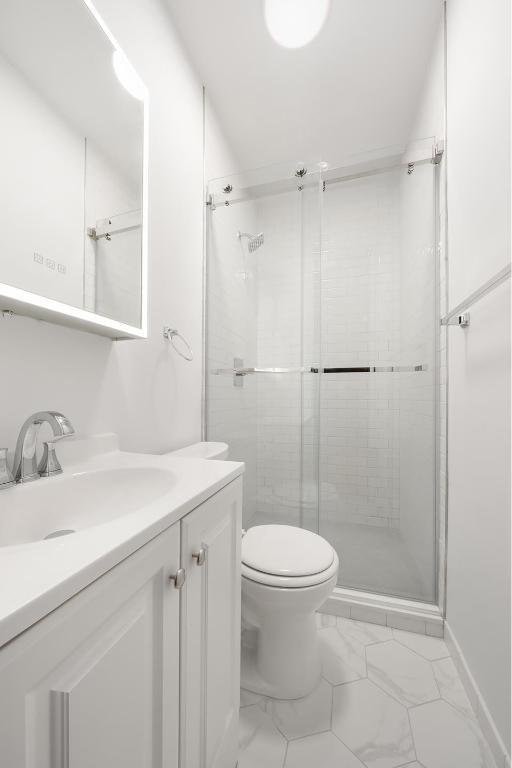 bathroom featuring a shower with door, vanity, and toilet