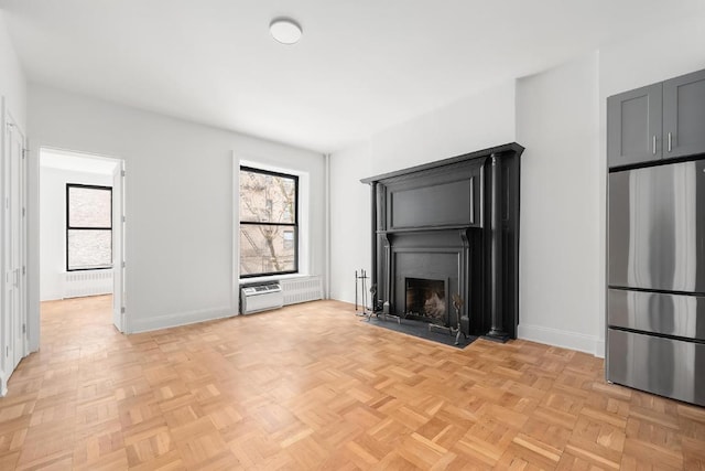 unfurnished living room featuring light parquet flooring, a healthy amount of sunlight, and radiator heating unit