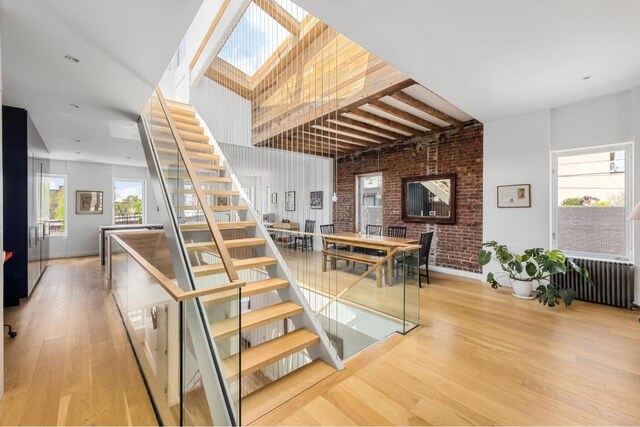 staircase with brick wall, radiator heating unit, a skylight, and hardwood / wood-style floors