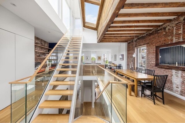 stairway with wood-type flooring, beamed ceiling, and brick wall