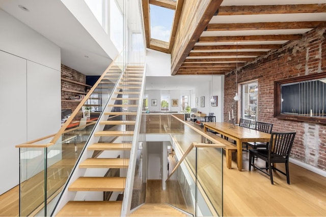 staircase featuring wood-type flooring, brick wall, and beam ceiling