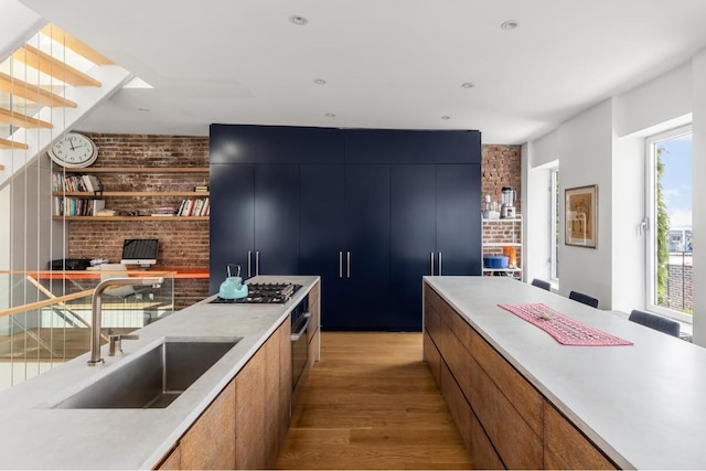 kitchen featuring stainless steel appliances, brick wall, sink, and light wood-type flooring