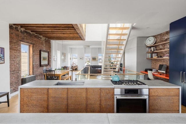 kitchen with brick wall, appliances with stainless steel finishes, sink, and a wealth of natural light