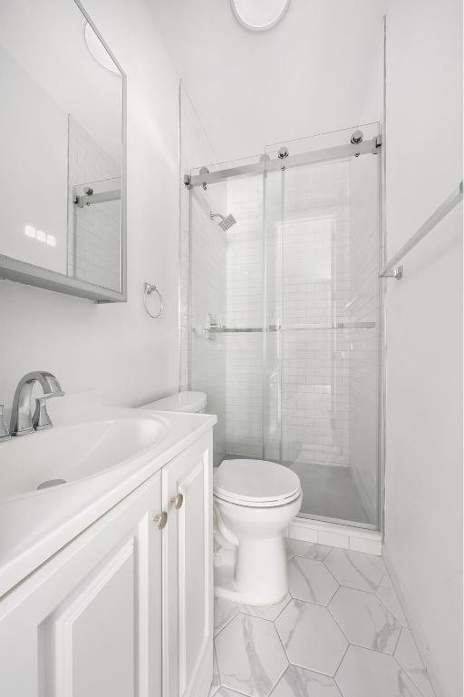 bathroom featuring vanity, a shower with shower door, and toilet