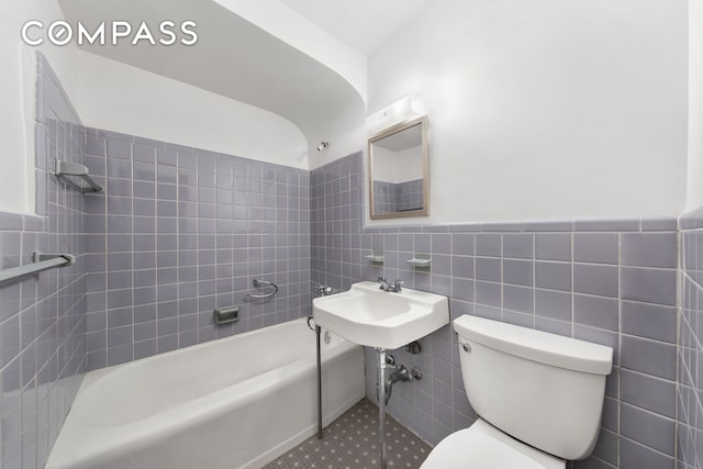 full bathroom featuring shower / washtub combination, toilet, wainscoting, tile walls, and a sink