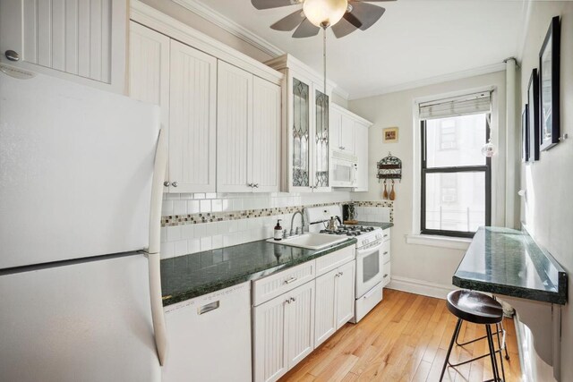 kitchen featuring sink, white cabinets, a kitchen bar, decorative backsplash, and white appliances