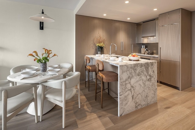 kitchen featuring a breakfast bar area, light stone countertops, light wood finished floors, recessed lighting, and modern cabinets