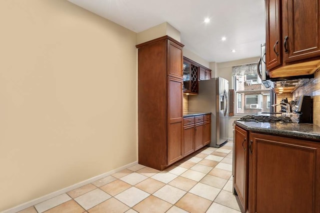 kitchen featuring stainless steel appliances, light tile patterned flooring, dark stone counters, and decorative backsplash