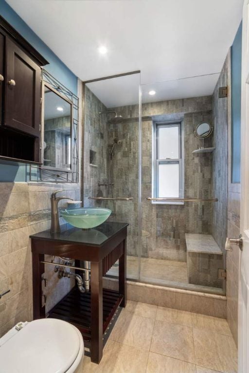 bathroom with tile walls, sink, a shower with door, and toilet