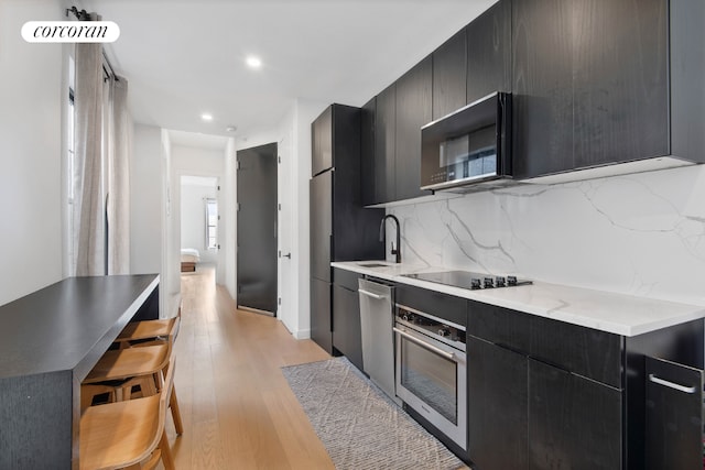 kitchen featuring sink, a kitchen breakfast bar, black appliances, light hardwood / wood-style floors, and decorative backsplash