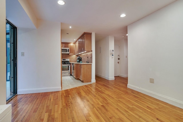 kitchen featuring brown cabinetry, light wood-style flooring, stainless steel appliances, light countertops, and backsplash