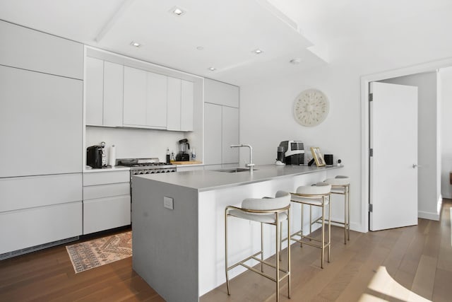 kitchen featuring a peninsula, a sink, dark wood finished floors, white cabinetry, and a kitchen bar