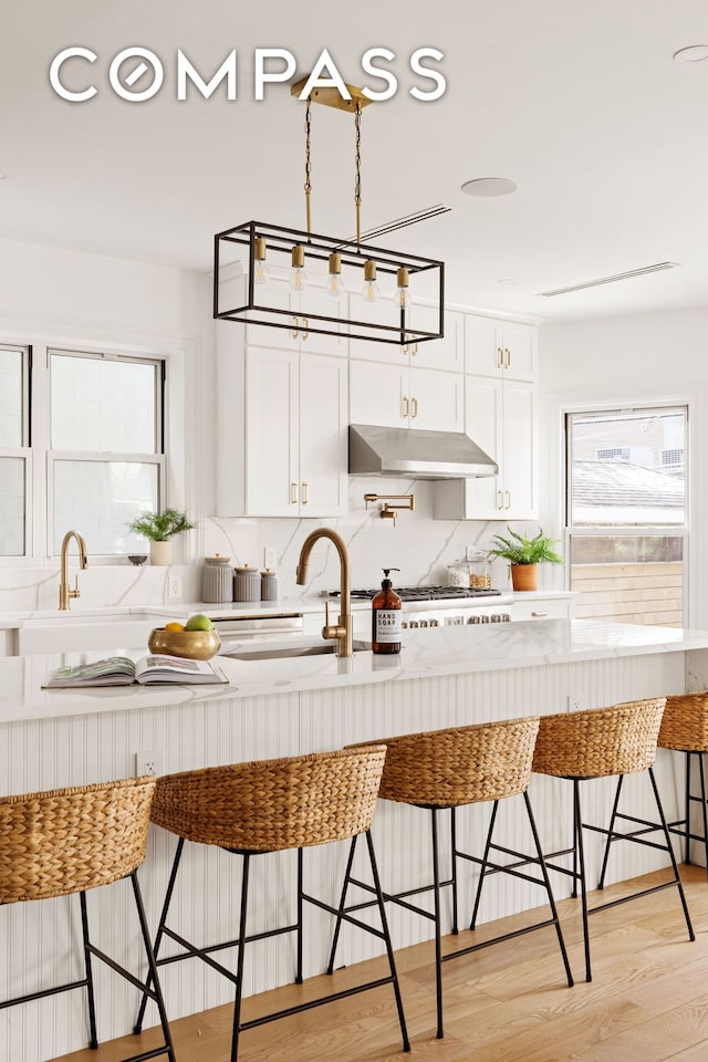 kitchen featuring a sink, a breakfast bar, under cabinet range hood, and white cabinetry