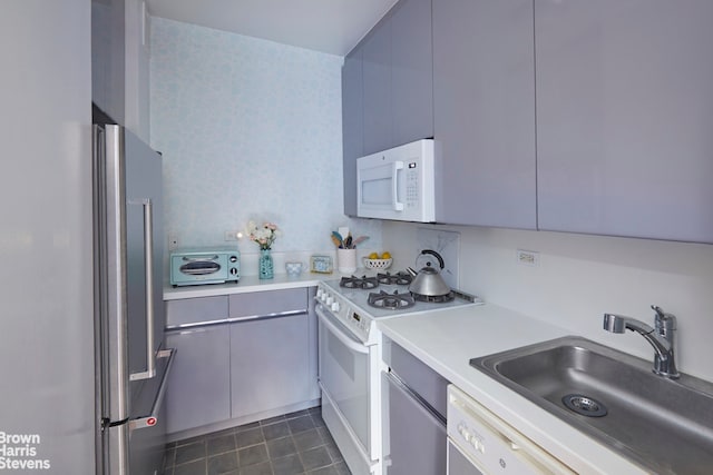 kitchen featuring white appliances, a toaster, dark tile patterned flooring, light countertops, and a sink