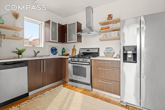 kitchen with sink, dark brown cabinets, light hardwood / wood-style flooring, stainless steel appliances, and wall chimney range hood