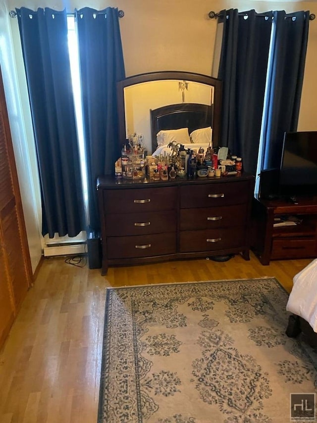 bedroom with a baseboard heating unit and light wood-style floors