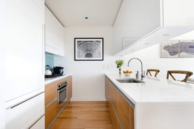 kitchen featuring appliances with stainless steel finishes, white cabinetry, sink, a kitchen breakfast bar, and light hardwood / wood-style flooring