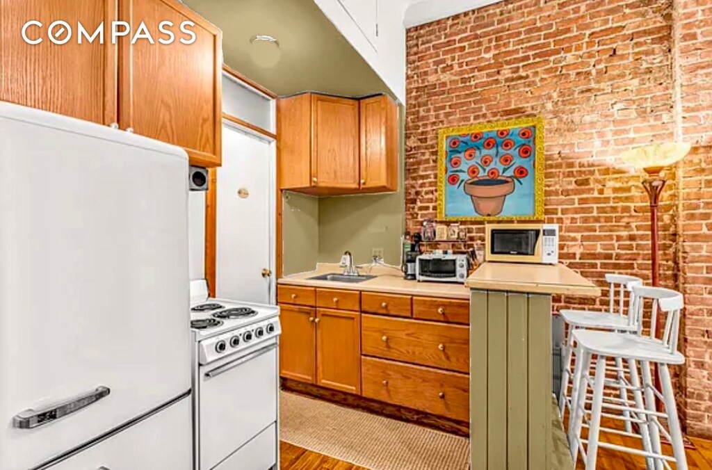 kitchen with brick wall, wood finished floors, a sink, light countertops, and white appliances
