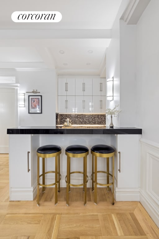 kitchen featuring a breakfast bar area, white cabinetry, kitchen peninsula, decorative backsplash, and light parquet floors