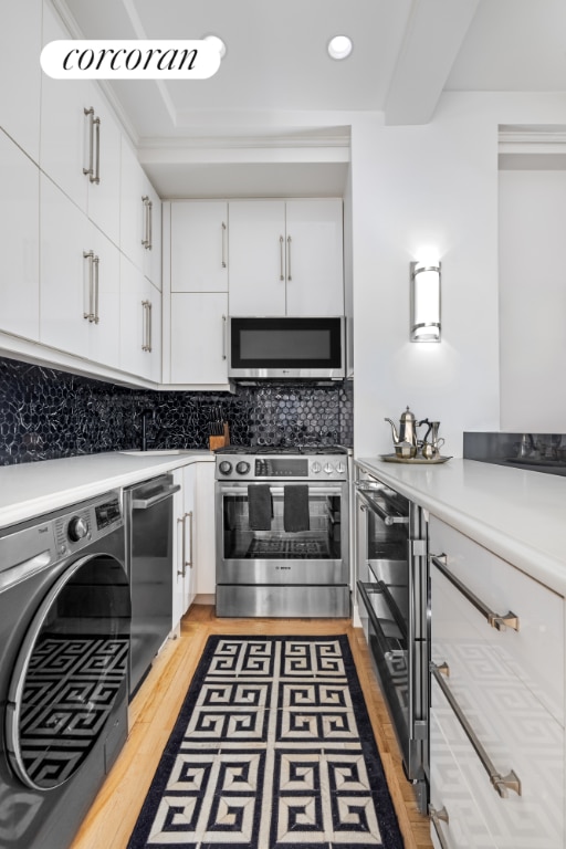 kitchen featuring hardwood / wood-style flooring, stainless steel appliances, tasteful backsplash, white cabinets, and washer / dryer