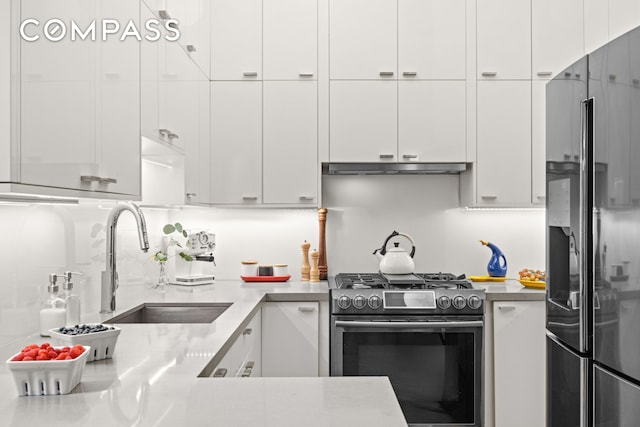 kitchen with black fridge, gas stove, a sink, white cabinets, and backsplash