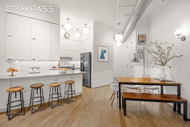 kitchen with decorative light fixtures, light hardwood / wood-style flooring, stainless steel fridge, kitchen peninsula, and white cabinets