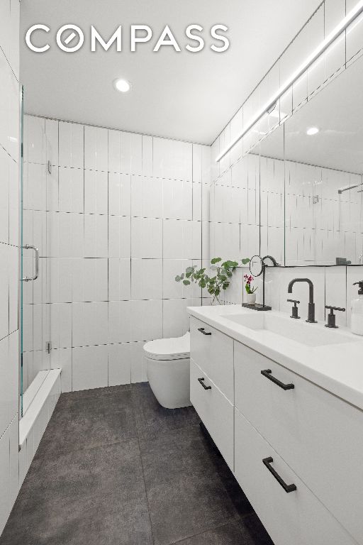 bathroom featuring a shower with door, vanity, tile walls, and toilet