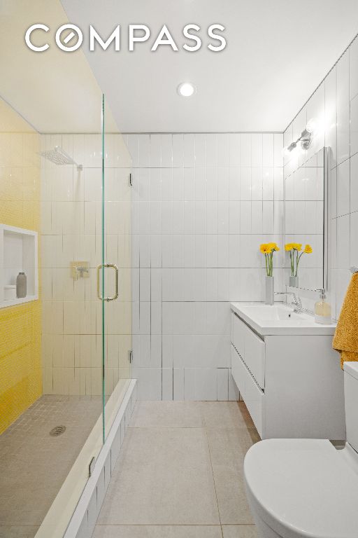 bathroom featuring a shower with door, tile walls, tile patterned floors, and toilet