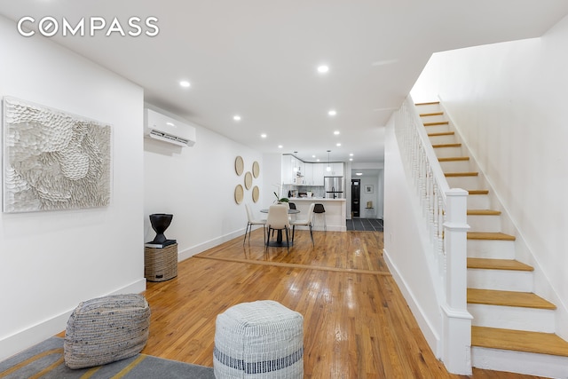 dining space with a wall mounted air conditioner, recessed lighting, stairway, light wood finished floors, and baseboards