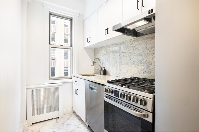 kitchen with radiator heating unit, white cabinetry, sink, stainless steel appliances, and plenty of natural light