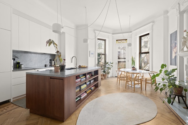 kitchen with white cabinetry, an island with sink, sink, backsplash, and light parquet flooring