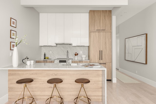 kitchen featuring modern cabinets, light wood finished floors, backsplash, and a kitchen bar