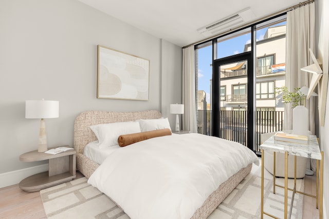 bedroom featuring access to outside, baseboards, wood finished floors, and floor to ceiling windows