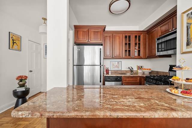 kitchen with sink, parquet floors, appliances with stainless steel finishes, kitchen peninsula, and light stone countertops