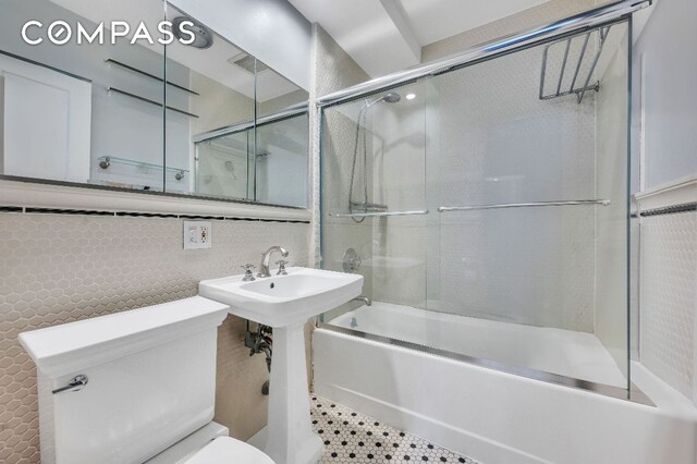 bathroom featuring tile walls, tasteful backsplash, combined bath / shower with glass door, and toilet