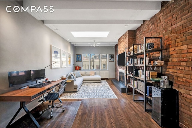 home office with dark wood-type flooring, beam ceiling, a skylight, a fireplace, and brick wall