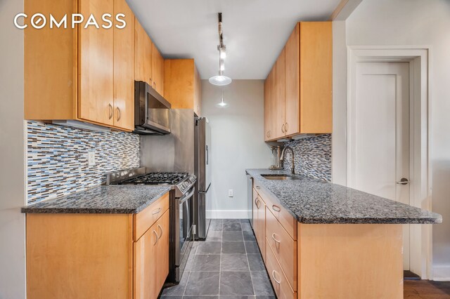 kitchen featuring sink, appliances with stainless steel finishes, tasteful backsplash, light brown cabinetry, and dark stone counters