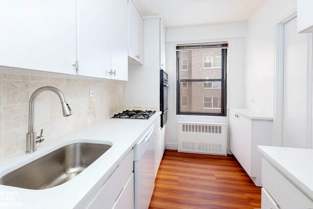 kitchen with backsplash, dishwasher, a sink, white cabinets, and radiator