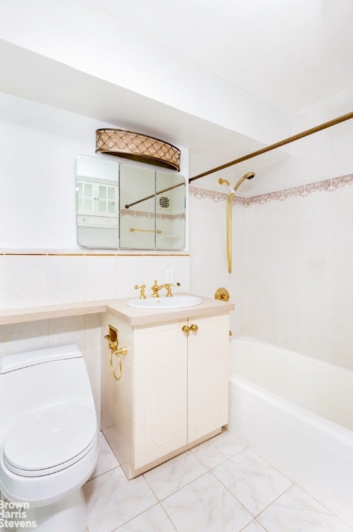 full bathroom with tile walls, vanity, tiled shower / bath combo, and toilet