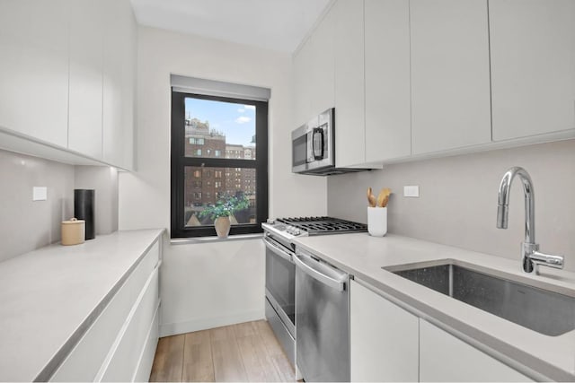 kitchen featuring white cabinetry, stainless steel appliances, sink, and light hardwood / wood-style flooring