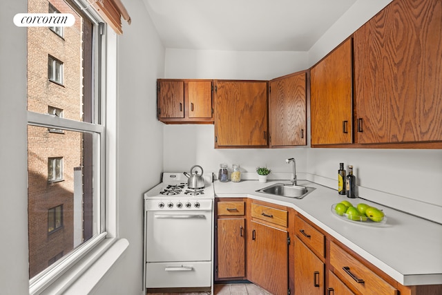 kitchen with brown cabinets, white range with gas stovetop, light countertops, and a sink