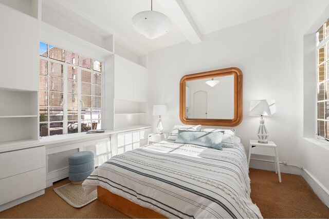 bedroom featuring beamed ceiling, multiple windows, and carpet