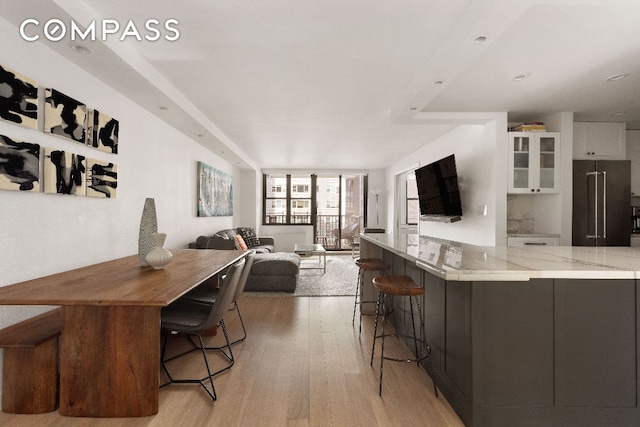 kitchen with high end fridge, light stone counters, light hardwood / wood-style flooring, a kitchen breakfast bar, and white cabinets