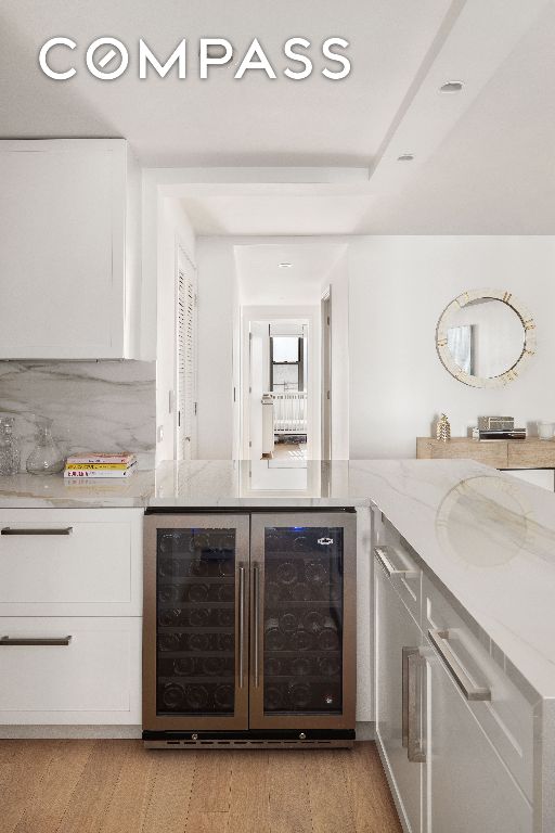 bar featuring light hardwood / wood-style flooring, backsplash, light stone countertops, white cabinets, and beverage cooler