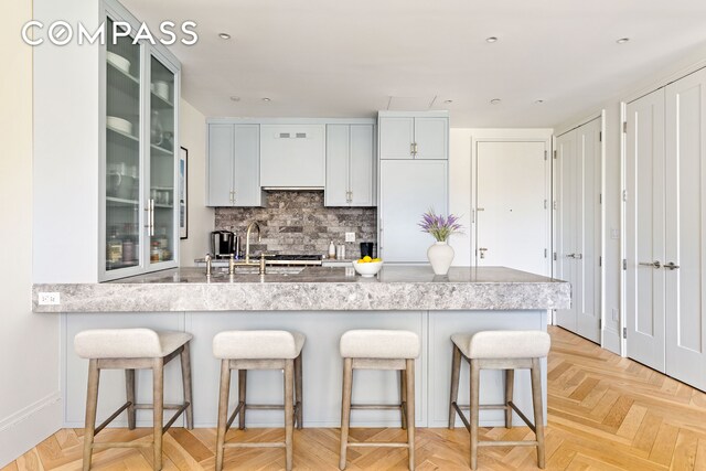 kitchen featuring tasteful backsplash, light countertops, glass insert cabinets, and a kitchen bar